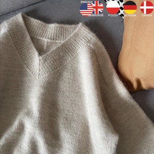 Könnte beinhalten: Ein hellbeiger V-Ausschnitt-Pullover aus weichem Strickstoff. Der Pullover ist gefaltet und auf einer braunen, strukturierten Oberfläche abgelegt.