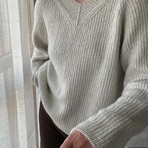 May include: A light gray knitted sweater with a V-neck and long sleeves.