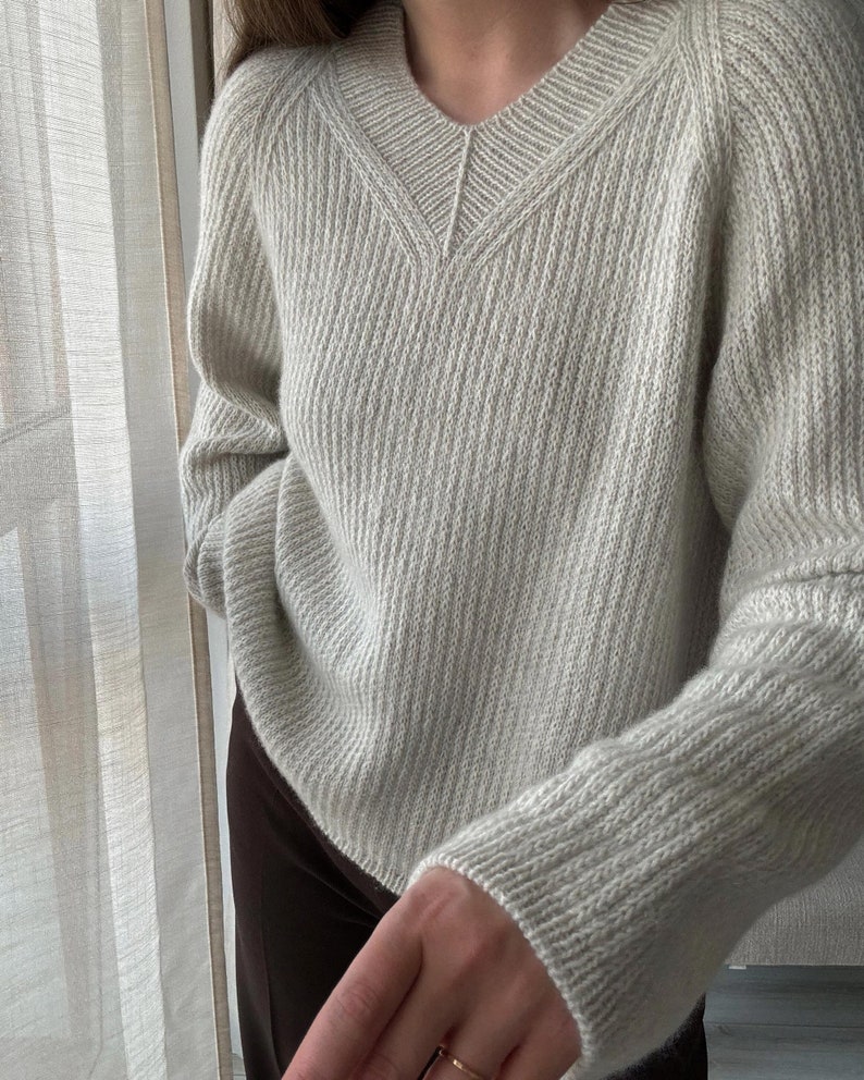 May include: A light gray knitted sweater with a V-neck and long sleeves.