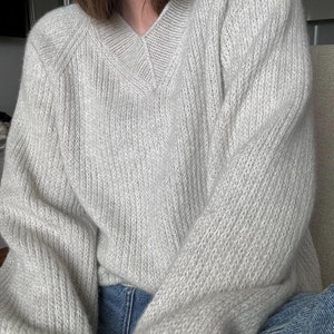 May include: A light gray knitted sweater with a v-neck and long sleeves. The sweater is made of a soft, fuzzy material.