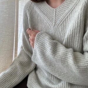May include: A light gray knitted sweater with a V-neck and long sleeves.
