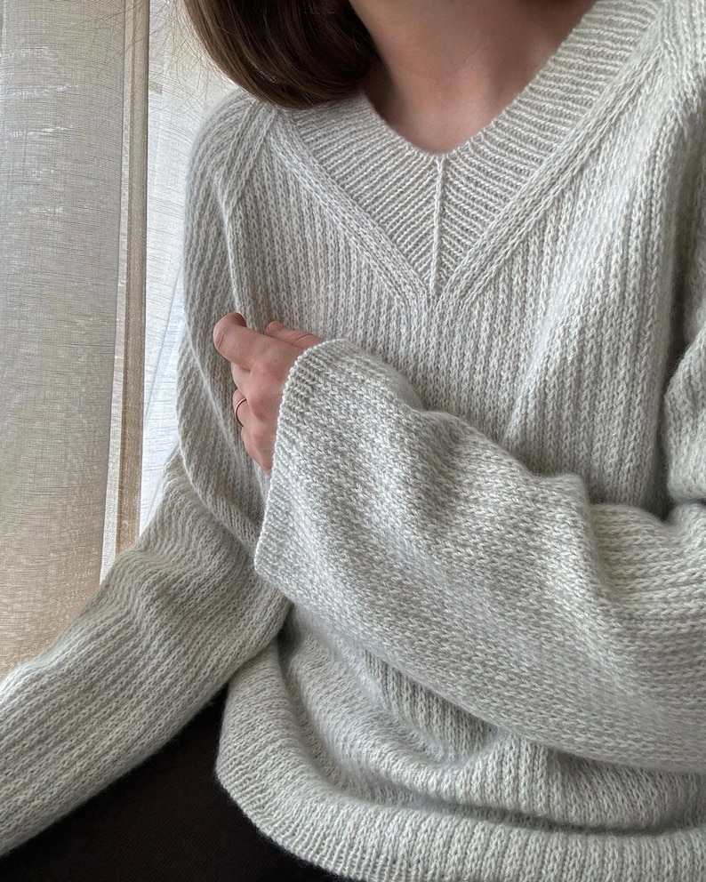 May include: A light gray knitted sweater with a V-neck and long sleeves.