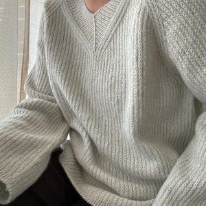May include: A light gray knitted sweater with a V-neck and long sleeves. The sweater has a ribbed texture.