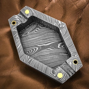 Könnte beinhalten: Ein sechseckiger Aschenbecher aus Metall mit einer gemusterten Oberfläche und goldenen Akzenten. Der Aschenbecher ist aus einem strapazierfähigen Material gefertigt und hat ein einzigartiges Design.