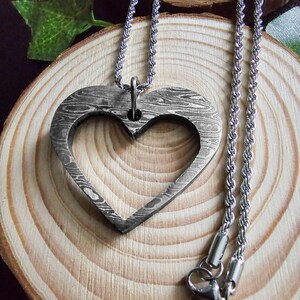 Pode incluir: Um colar de prata com um pingente em forma de coração e uma corrente de corda. O pingente tem um design texturizado detalhado.