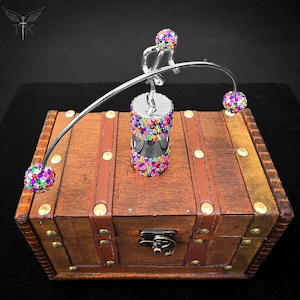 May include: A decorative silver sculpture of a person balancing on a curved bar, with colourful jeweled spheres at each end and on the base. The sculpture sits atop a wooden treasure chest with leather straps and brass studs. The chest is approximately 30 cm long.