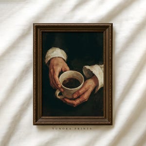 May include: A framed print depicting a vintage painting of hands cradling a coffee cup. The artwork has a dark, atmospheric style, set within a brown frame. The text "YUNORA PRINTS" is visible at the bottom.