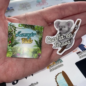 May include: A set of colorful stickers with inspirational messages in Spanish. The stickers feature a koala, a jungle scene, and the phrases "La Mejor Vida" and "Confia en Jehova".