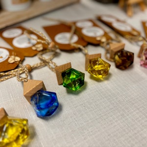 May include: A set of colourful glass and wood car air fresheners. Each air freshener is shaped like a geometric crystal and hangs from a string.