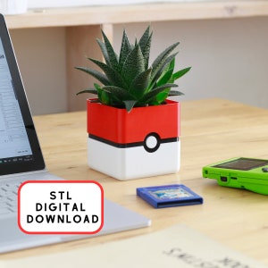 Può includere: Un vaso da fiori stampato in 3D a forma di Poké Ball, con la parte superiore rossa e quella inferiore bianca. Il vaso è pieno di una pianta grassa verde. Il vaso è su un tavolo di legno accanto a un laptop e una cartuccia di gioco.