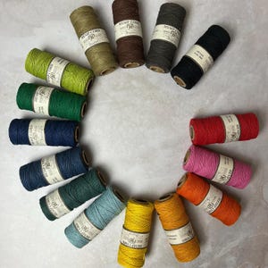 May include: A selection of colourful hemp cords with labels that read "Hemp Cord" in various fonts and colours. The cords are arranged in a circle on a light grey surface.