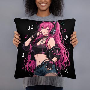 Può includere: Un cuscino quadrato con sfondo nero raffigurante un personaggio in stile anime dai lunghi capelli rosa, che indossa cuffie nere con logo, un top corto nero e pantaloncini di jeans, circondato da note musicali e piccoli cuori fluttuanti.