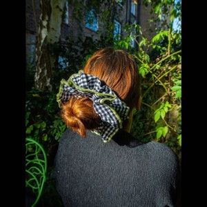 May include: A black and white gingham scrunchie with a lime green trim. The scrunchie is tied around a woman's hair.