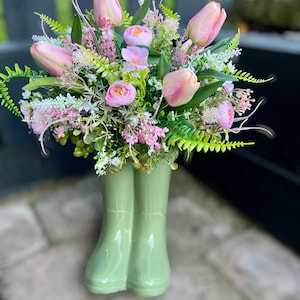 May include: A bouquet of pink tulips and other flowers arranged in a green ceramic boot vase.