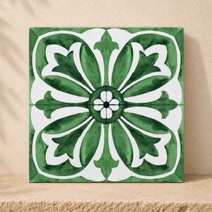 May include: A square ceramic tile featuring a symmetrical floral pattern in deep forest green and white. The design consists of four large, stylized petal shapes radiating from a central white flower with a dark center, set against a white background.