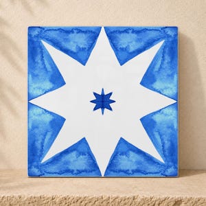 Puede incluir: Un azulejo cuadrado de cerámica con una estrella blanca de ocho puntas sobre un fondo azul estilo acuarela. Una estrella azul sólida más pequeña de ocho puntas está centrada dentro de la estrella blanca, creando un contraste geométrico.