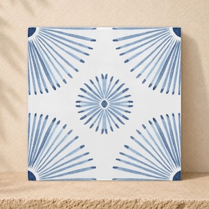 Pode incluir: Um azulejo quadrado de cerâmica com fundo branco e um padrão azul repetitivo. O design consiste num motivo central circular de raios de sol rodeado por quatro raios parciais nos cantos, tudo representado em tons de azul.