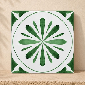 Könnte beinhalten: Eine quadratische Keramikfliese mit weißem Hintergrund und einem mittig platzierten dunkelgrünen Blumenmotiv. Das Design besteht aus einer kreisförmigen Umrandung, die ein symmetrisches Muster aus zwölf länglichen Blütenblättern umschließt.