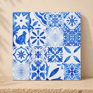 Könnte beinhalten: Eine quadratische dekorative Fliesenplatte mit einem Raster aus sechzehn einzelnen Quadraten mit blau-weißen Aquarellmustern. Die Designs umfassen geometrische Sterne, florale Motive und Silhouetten von Katzen auf weißem Hintergrund.