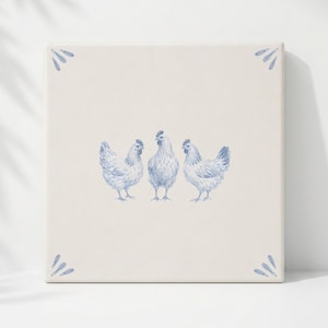May include: A square ceramic tile with a cream-coloured background featuring a blue painted illustration of three chickens standing side by side in the centre, accented by small blue leaf-like motifs in each of the four corners of the tile.