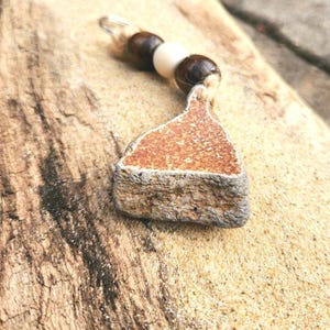 May include: A brown, triangular, stone pendant with a rough texture, hanging from a string with brown and white beads.