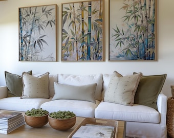 May include: Three framed bamboo art prints in shades of green, blue, and beige hang above a white sofa with decorative pillows. A wooden coffee table displays moss-filled bowls and a woven tray with books, creating a serene living room setting.