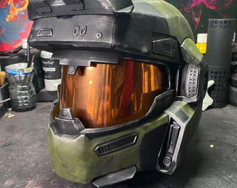 Op de afbeelding: Een groene en zwarte helm met een vizier en een zwart vizier. De helm heeft een getextureerd oppervlak en een zwart vizier. De helm heeft een zwart vizier en een zwart vizier.