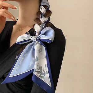Puede incluir: Una bufanda azul y blanca con estampado floral con el texto "Me encanta el verano y el aroma de las flores" atada alrededor del cuello de una persona.