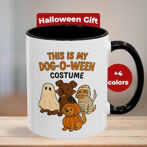 Può includere: Tazza in ceramica bianca con manico e interno neri. La tazza presenta il testo "THIS IS MY DOG-O-WEEN COSTUME" e illustrazioni di cani vestiti con costumi di Halloween. Un'etichetta rossa dice "Halloween Gift".