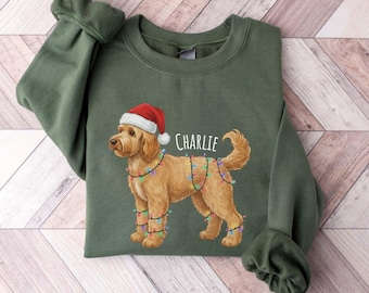 Può includere: Felpa verde con un cane golden doodle con cappello di Babbo Natale e luci colorate. Il nome del cane, "Charlie", è stampato sopra. La felpa ha maniche lunghe ed è realizzata in materiale morbido.
