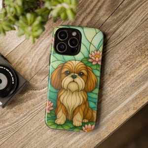Könnte beinhalten: Eine Handyhülle mit einem Cartoon-Design eines Shih Tzu-Hundes. Die Hülle hat einen Hintergrund im Glasmalerei-Stil mit rosa und grünen Seerosen. Der Hund ist braun und hellbraun mit einem langen, flauschigen Bart.