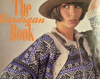 May include: A book cover titled The Cardigan Book featuring a person wearing a brown felt hat and a long-sleeved knit cardigan with a blue, black, and white geometric pattern, a beige collar, and a buttoned placket. The text Nitmaster 2000 is visible.