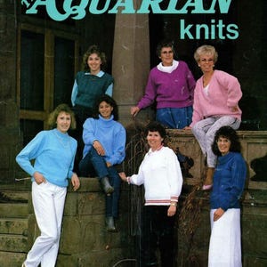 May include: A magazine cover with the text "The Aquarian Knits" in teal. The image shows a group of women wearing knit sweaters in blue, pink, purple, and white. The women are posing on a stone structure, showcasing the knitwear.