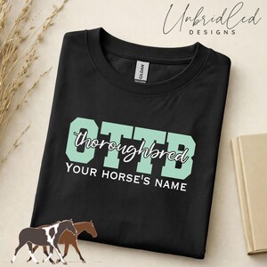 May include: A black t-shirt featuring the large mint green block letters OTTB with the word thoroughbred written in white cursive script across the center and the text YOUR HORSE'S NAME printed in white below the graphic design.