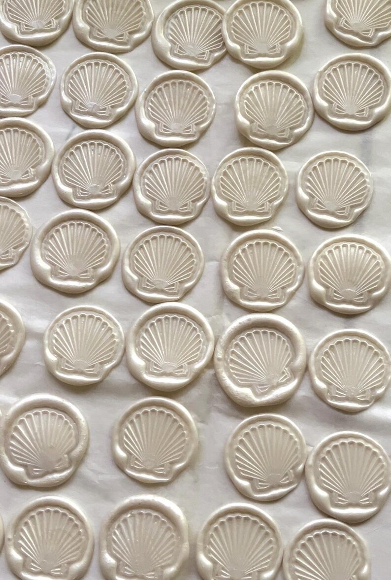 K&ouml;nnte beinhalten: Eine Ansammlung von cremewei&szlig;en Wachssiegeln, die jeweils ein detailliertes Muscheldesign aufweisen. Die Siegel sind eng angeordnet und bilden ein Muster. Das Muscheldesign umfasst strahlenf&ouml;rmige Linien und eine Schleife.