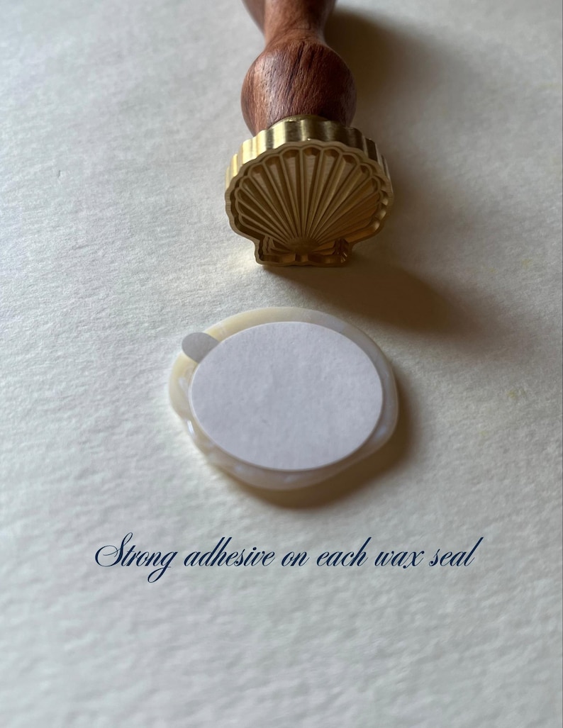 K&ouml;nnte beinhalten: Ein muschelf&ouml;rmiger Wachssiegelstempel mit Holzgriff, neben einem Wachssiegel mit wei&szlig;em Klebeaufkleber. Der Text "Strong adhesive on each wax seal" ist sichtbar.