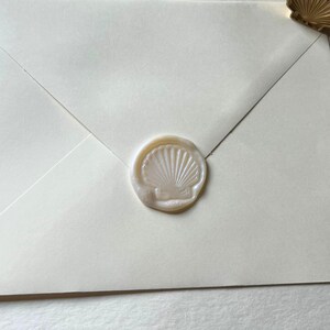K&ouml;nnte beinhalten: Elfenbeinfarbener Umschlag mit einem Muschel-Wachssiegel. Der Stempel hat eine helle, perlmuttartige Farbe, und der Umschlag ist ein weiches Off-White. Das Wachssiegel ist mittig platziert und erzeugt einen klassischen und eleganten Look.