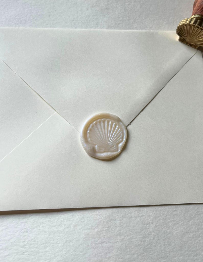 K&ouml;nnte beinhalten: Elfenbeinfarbener Umschlag mit einem Muschel-Wachssiegel. Der Stempel hat eine helle, perlmuttartige Farbe, und der Umschlag ist ein weiches Off-White. Das Wachssiegel ist mittig platziert und erzeugt einen klassischen und eleganten Look.