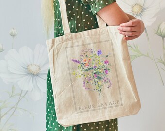 Könnte beinhalten: Eine weiße Canvas-Tragetasche mit einem Blumendesign und dem Text "Fleur Savage".