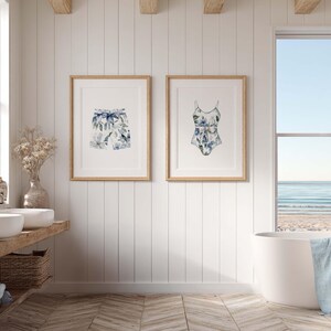Add a touch of coastal elegance to your home with this coordinated set of two floral swimwear watercolor prints. Featuring a matching one-piece swimsuit and swim trunks adorned with soft blue florals and botanical accents, this collection blends vintage beach charm with sophisticated coastal style. Perfect for bathrooms, beach houses, lake cottages, dressing rooms, pool houses, and summer-inspired interiors.