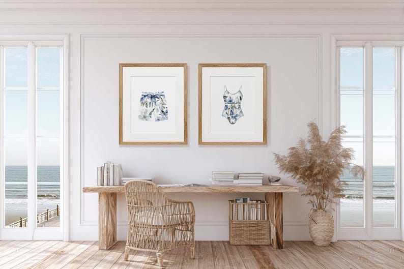 Add a touch of coastal elegance to your home with this coordinated set of two floral swimwear watercolor prints. Featuring a matching one-piece swimsuit and swim trunks adorned with soft blue florals and botanical accents, this collection blends vintage beach charm with sophisticated coastal style. Perfect for bathrooms, beach houses, lake cottages, dressing rooms, pool houses, and summer-inspired interiors.