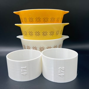 May include: Three yellow and white ceramic bowls with a brown star pattern stacked on top of each other. Two white plastic rings with the number 472 printed on them are in front of the bowls.