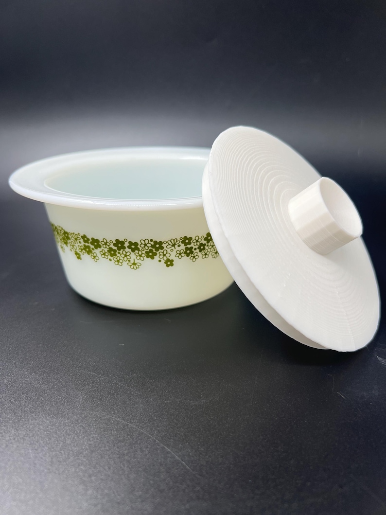 May include: White ceramic bowl with a green floral pattern and a matching lid. The lid has a raised knob on top.