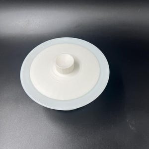May include: White ceramic bowl with a lid. The bowl has a smooth, white glaze and a slightly rounded shape. The lid has a small knob on top.
