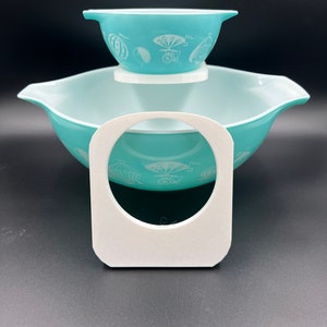 May include: Two turquoise blue mixing bowls with a white floral design. The smaller bowl is stacked on top of the larger bowl.