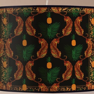 Può includere: Paralume nero con un motivo ripetitivo di leopardi arancioni, foglie di palma verdi e ananas gialli.