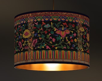 May include: A cylindrical lampshade with a black background and a colorful floral pattern. The design includes pink, yellow, and blue flowers with green leaves. The top and bottom edges have decorative borders. The interior is gold.