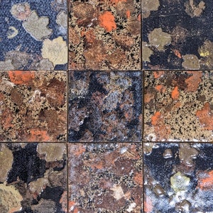 May include: Nine square ceramic tiles with a mottled, abstract design in shades of black, brown, orange, and gold.