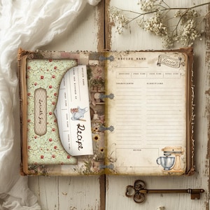 May include: Open recipe book with a vintage aesthetic. The book features a floral patterned pocket with the text "Sprinkle Joy." A recipe card is inserted, and the right page has space for ingredients and directions. A key lies below.