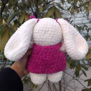 May include: White crocheted bunny wearing a pink dress. The bunny has long floppy ears and a sweet expression.